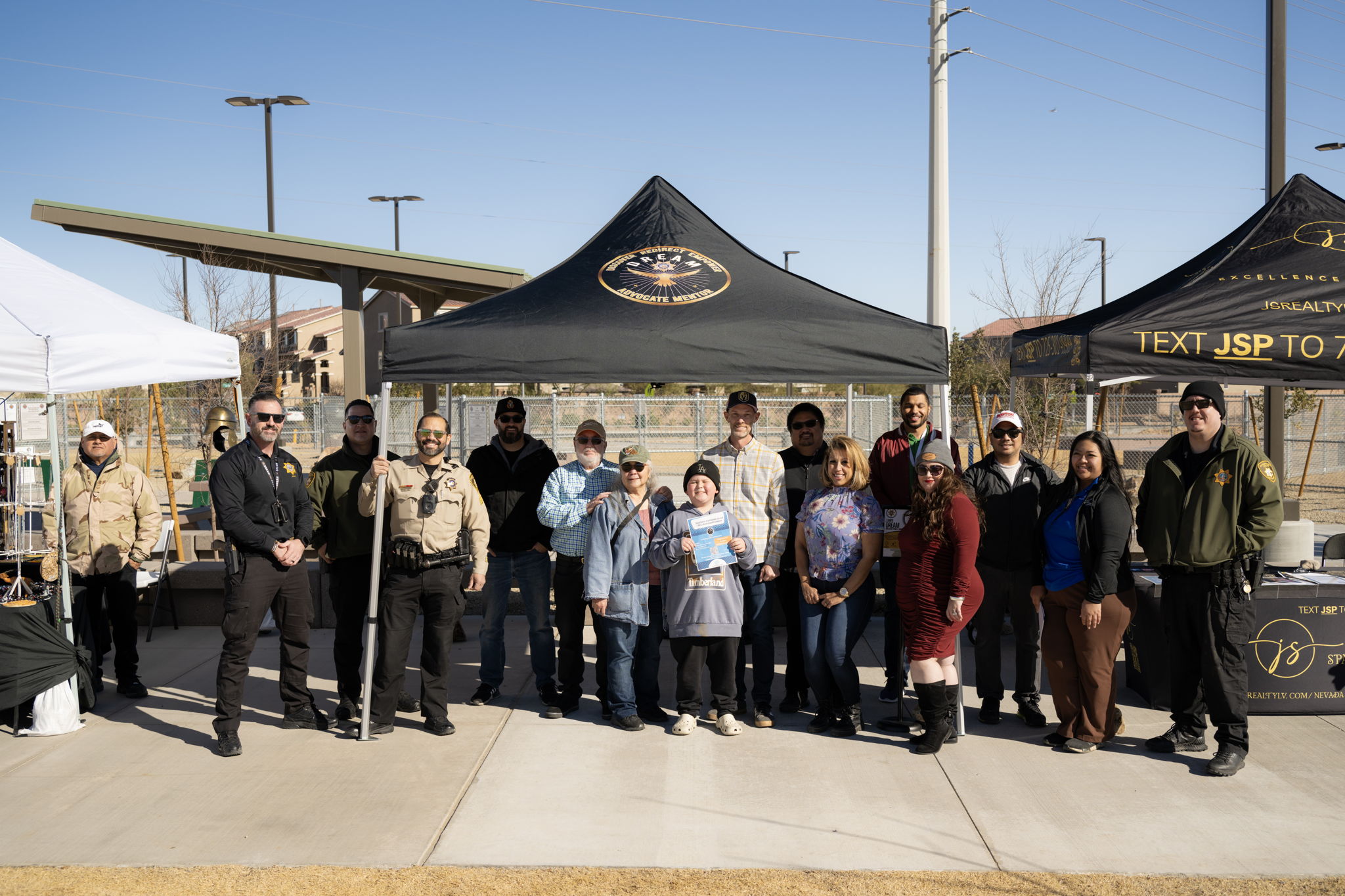 Community members and law enforcement pose together at an outdoor event, showcasing collaboration and engagement in neighborhood initiatives.