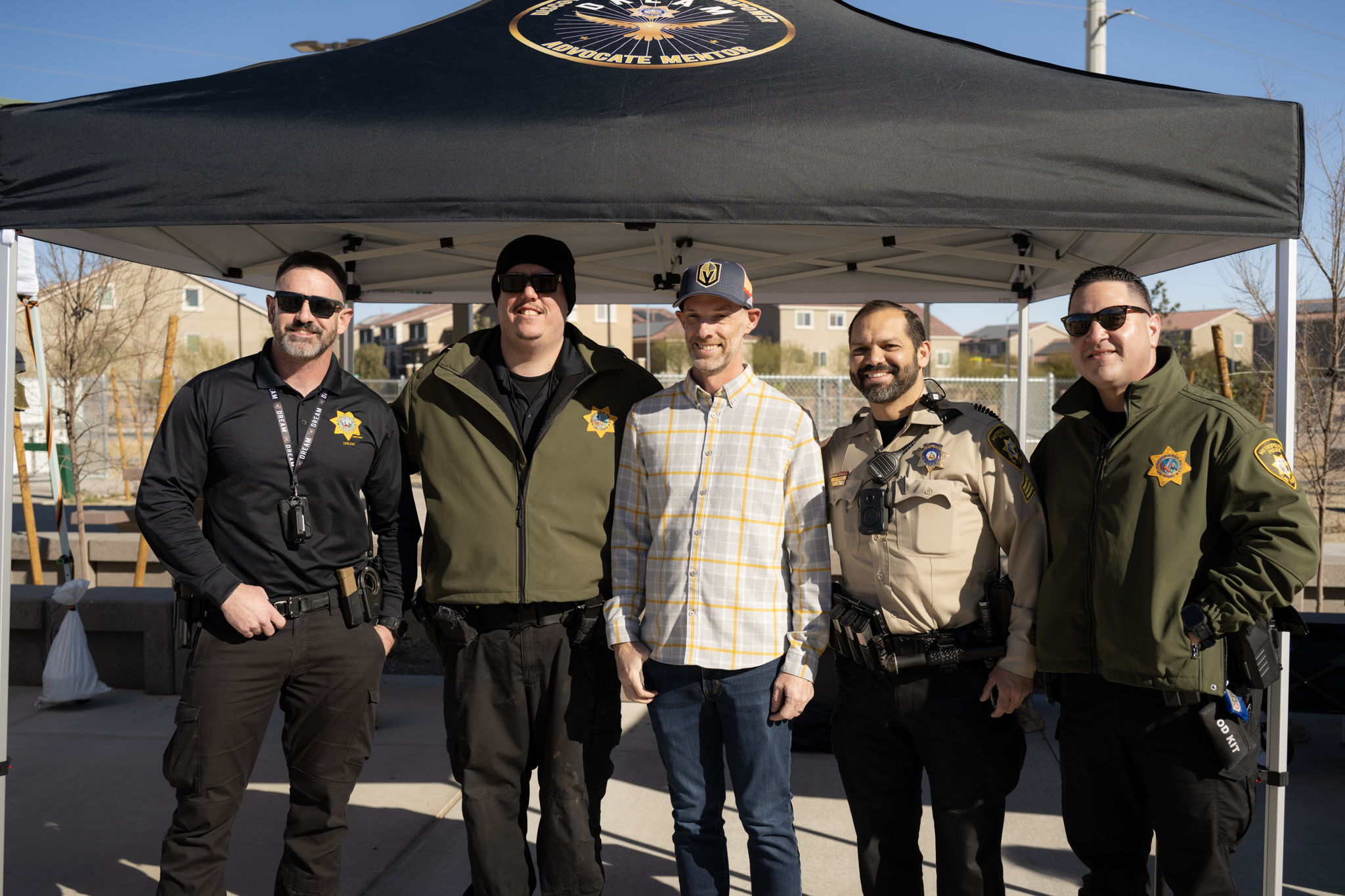 Community safety event featuring law enforcement officers posing together with an organizer under a canopy, promoting engagement and support.