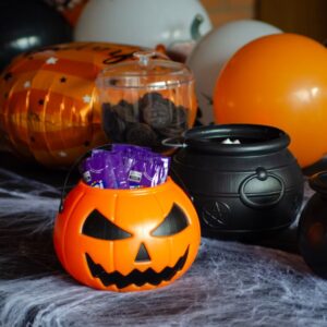 Halloween themed candy display with a pumpkin bucket and cauldrons on a decorated table.