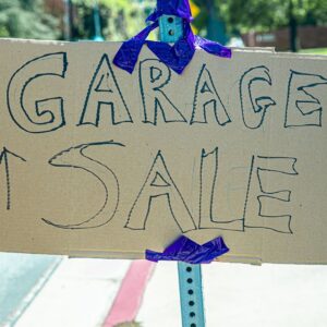 A handwritten garage sale sign taped on cardboard, displayed outdoors.